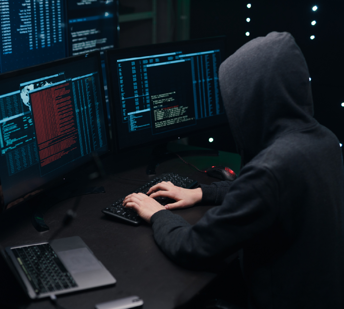 Hooded hacker in front of computer screens