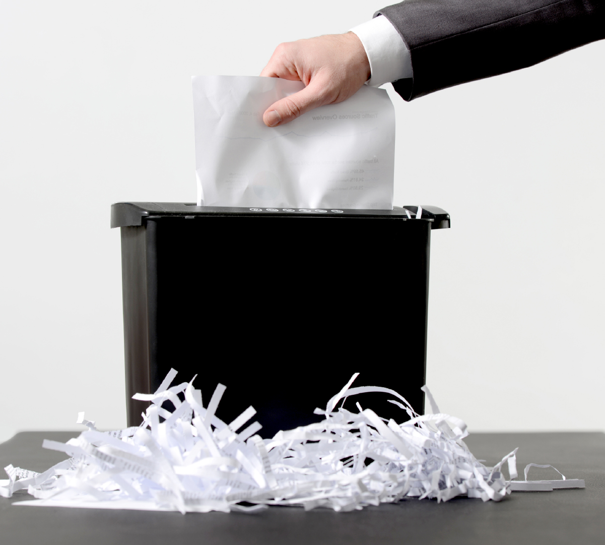 Person entering a piece of paper into a shredder placed on a table.