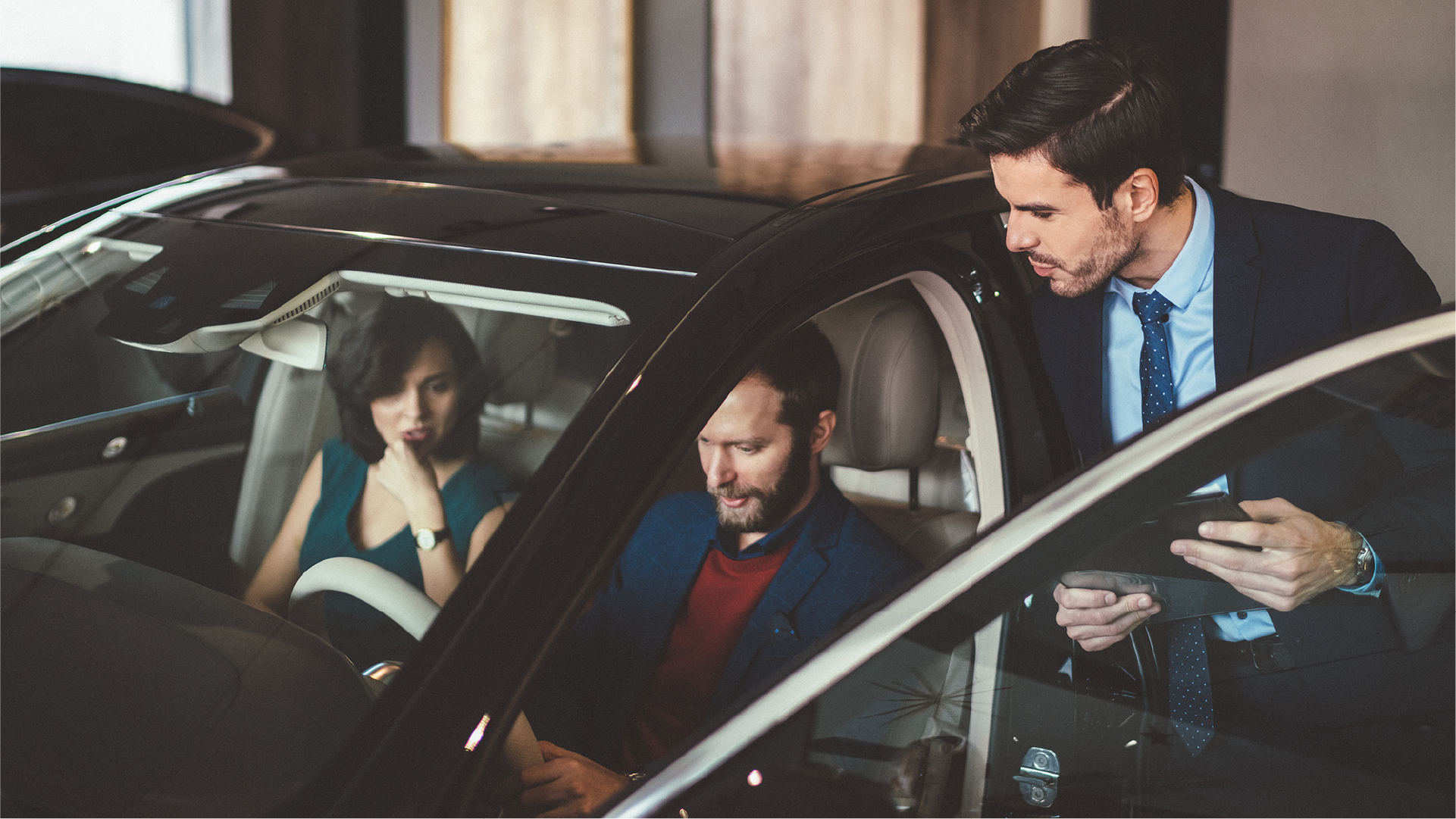 Decorative image: A car salesperson talking to two customers sitting in the front of a car they are considering buying.